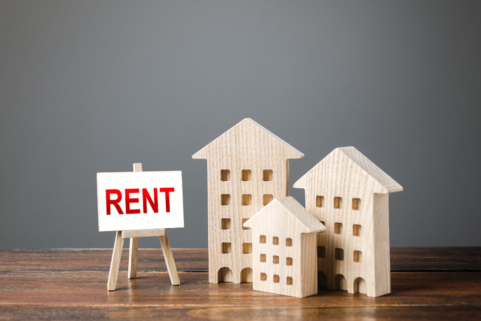 A graphic of three wooden replicas of apartment buildings with a white sign with the word "rent" in red letters next to them.